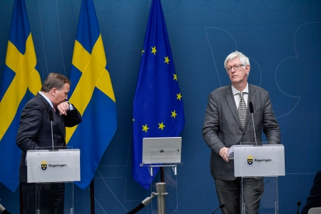 Sveriges statsminister Stefan Löfven hoster i armkroken under en pressekonferanse om koronapandemien i mai. Ved siden av står Johan Carlson, generaldirektør for Folkhälsomyndigheten.